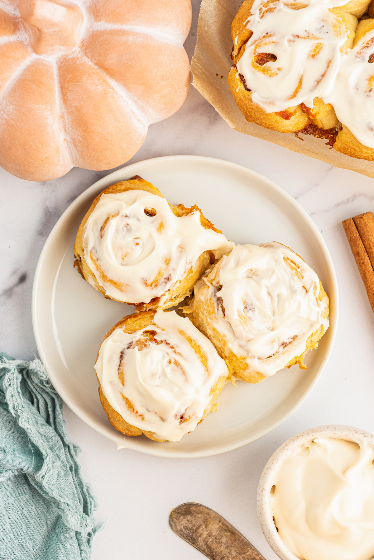 Three frosted pumpkin cinnamon rolls on a plate.