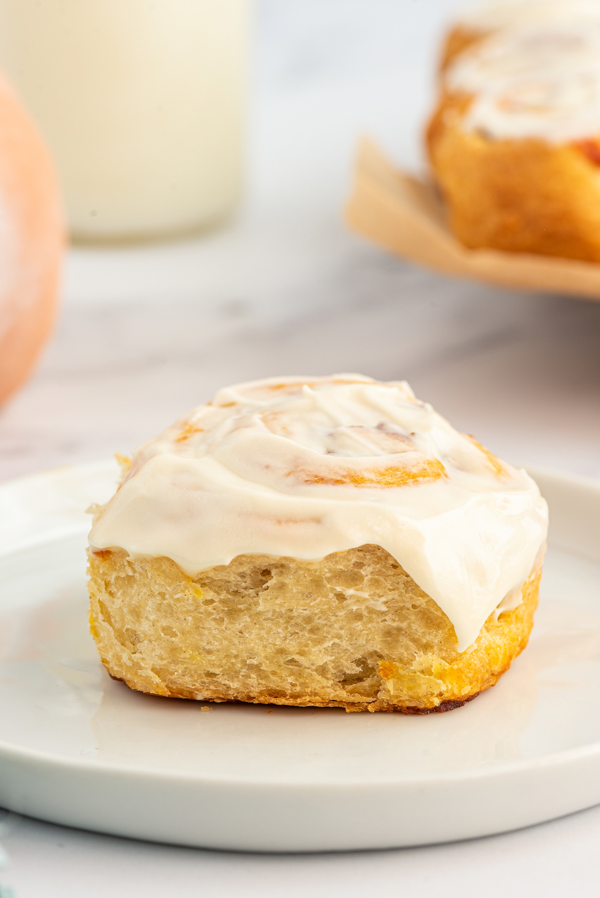 One frosted pumpkin cinnamon roll on a plate.