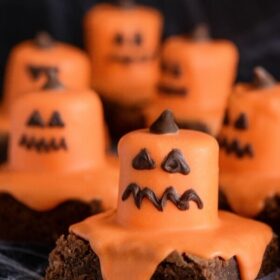 Six Melted Jack O' Lantern Brownies on a Black Surface Covered in Fake Spider Webs