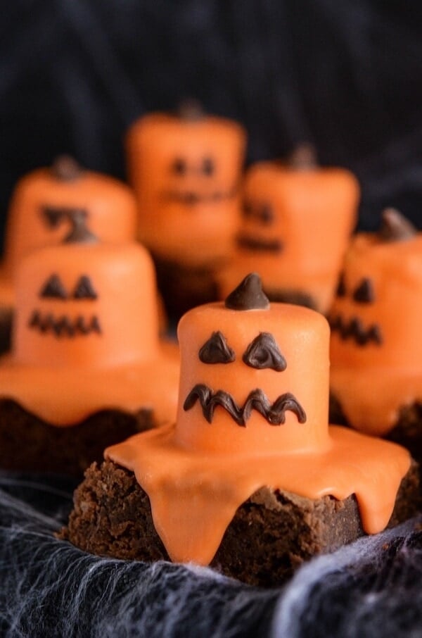 Six Melted Jack O' Lantern Brownies on a Black Surface Covered in Fake Spider Webs