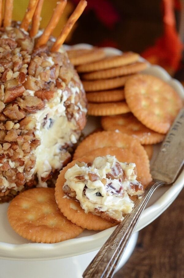 A cracker topped with a portion of a cheeseball, on a plate filled with crackers surrounding a Turkey Cheese Ball.