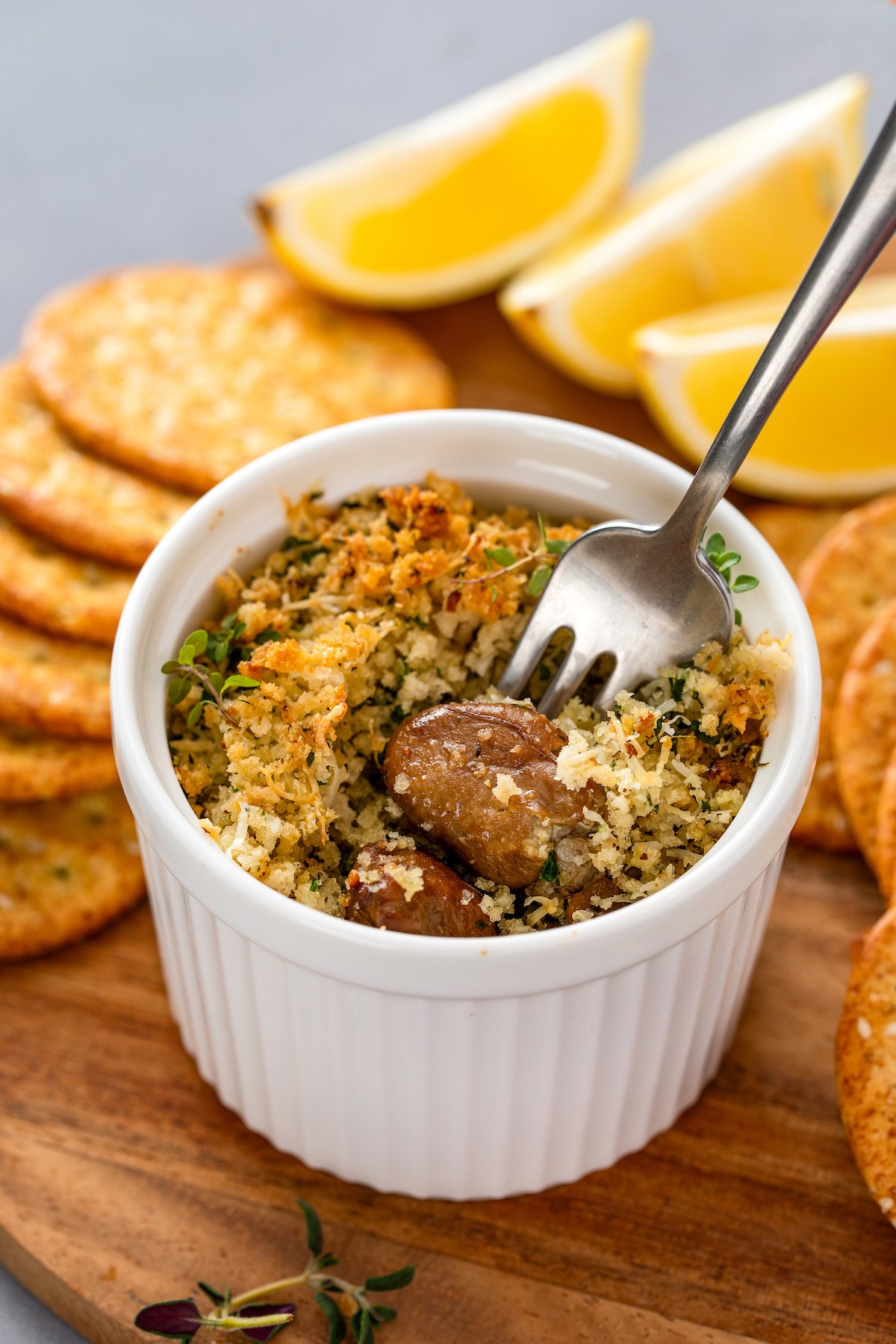 A baked oyster with buttery parmesan breadcrumbs is being lifted from a ramekin. 