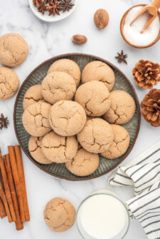 Overhead shot of a dozen or so cookies on a serving pate, with cinnamon sticks and pinecones arranged on the table.
