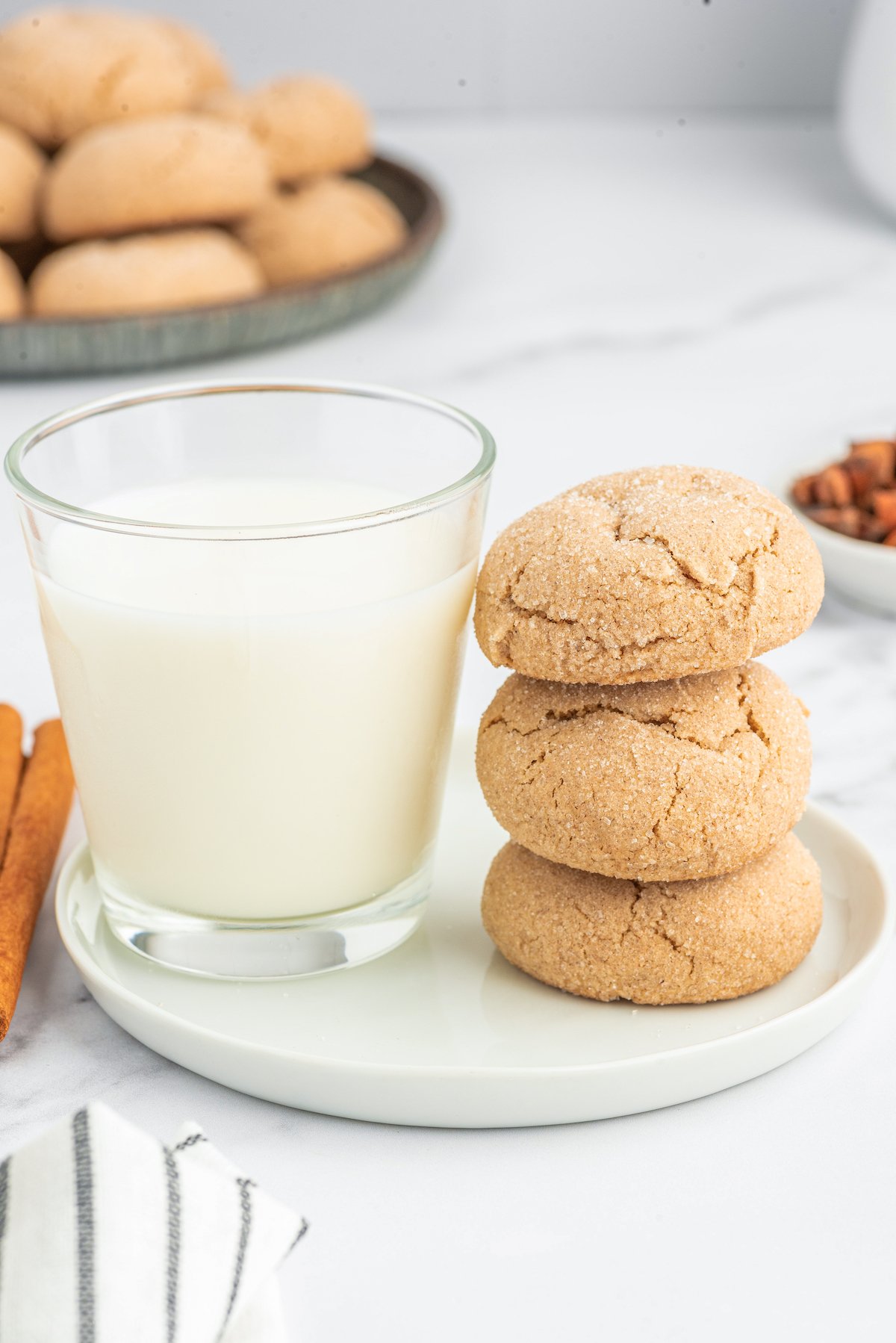 Three cookies balanced on top of each other, next to a glass of milk.