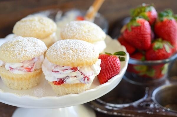 Four strawberries and cream cupcakes on a cake stand garnished with a fresh strawberry.