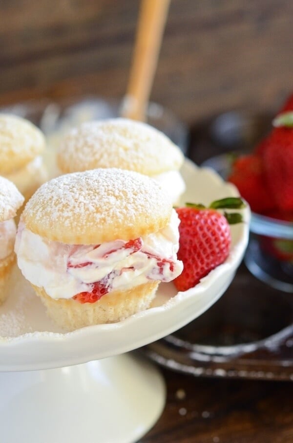 Strawberries and cream cupcakes on a cake stand garnished with a fresh strawberry.