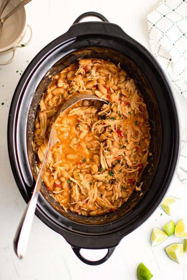 Crock pot white chicken chili inside the slow cooker with a serving spoon.