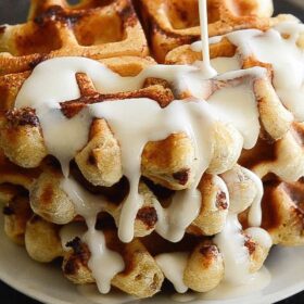 A Stack of Cinnamon Roll Waffles being Drizzled with Maple Cream Cheese Syrup