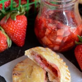 Strawberries and Cream Hand Pies with whole strawberries on a dark surface with a jar of macerated strawberries