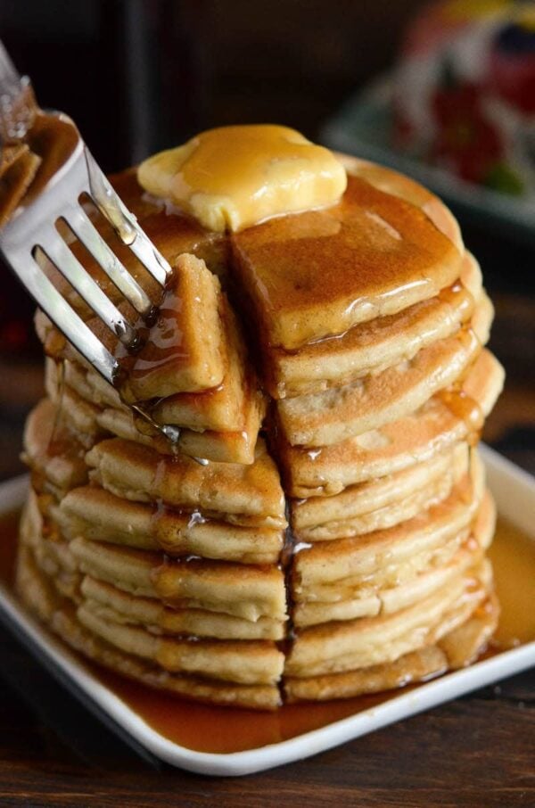 A stack of Low Carb Keto Pancakes with butte rand syrup and a bite being taken out of them.