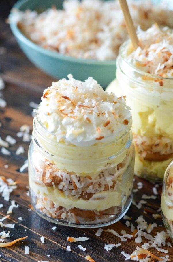 Close up of a small mason jar filled with layers of vanilla pudding, vanilla wafers and toasted coconut.
