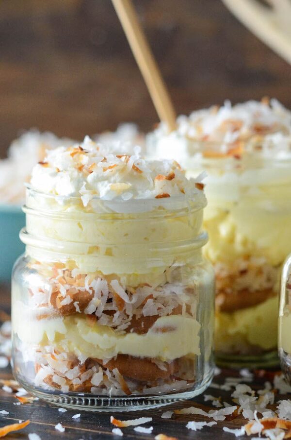 Side view of a small jar filled with nilla wafers, vanilla pudding and toasted coconut.