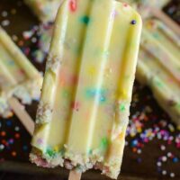 A Funfetti Cake Pudding Pop Being Held Above a Baking Sheet Holding More Popsicles