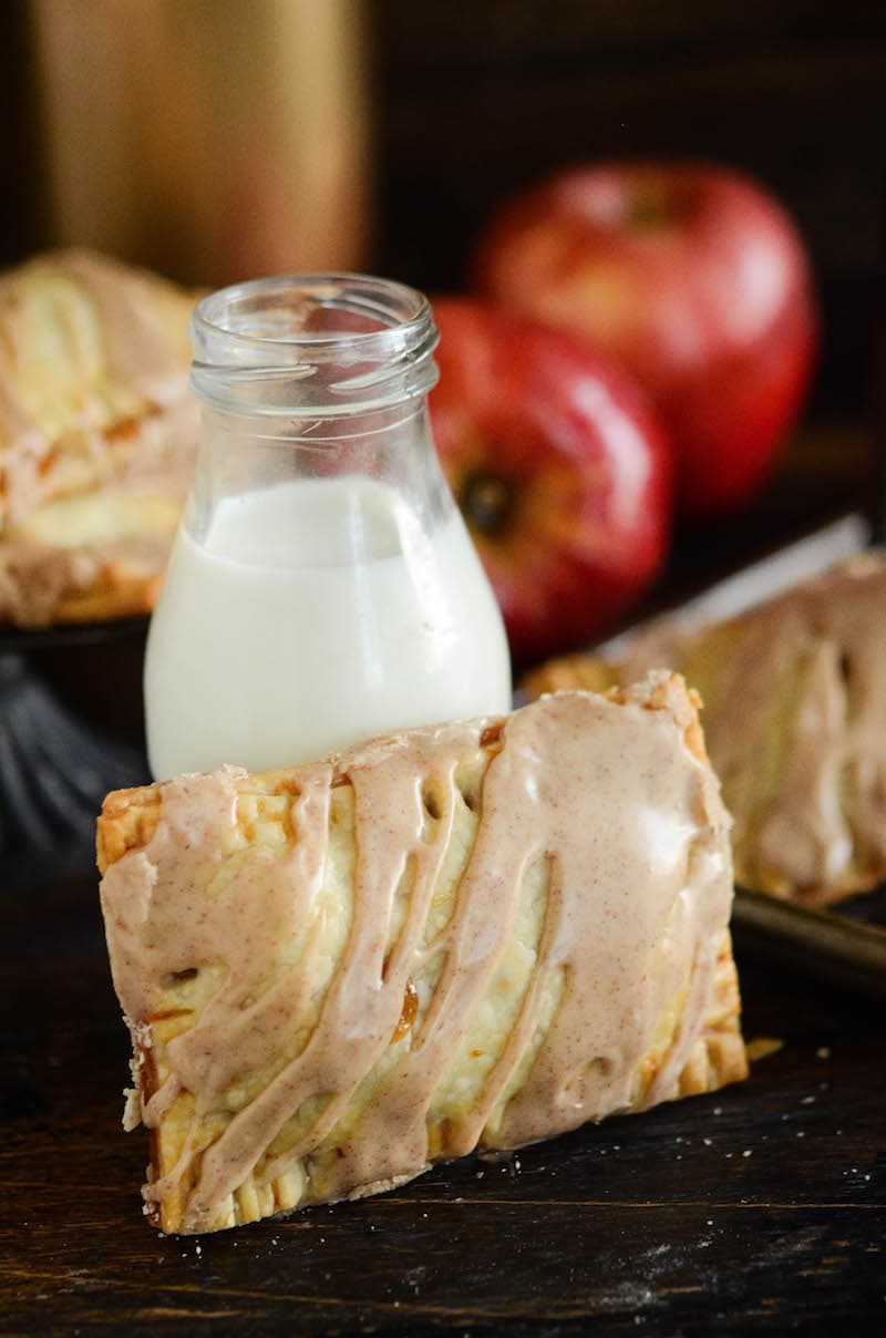 An apple pie Poptart with cinnamon icing laid against a bottle of milk.
