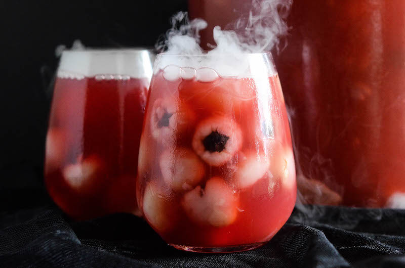 Glasses of sparkling cranberry halloween eyeball punch with floating lychees, garnished with dry ice.