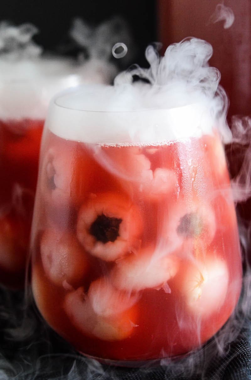 Glasses of sparkling cranberry halloween eyeball punch with floating lychees, garnished with dry ice.