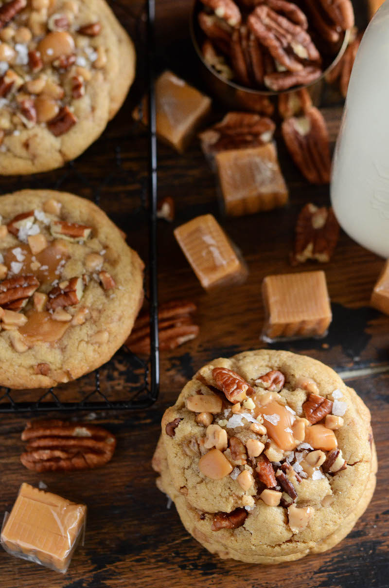 Three salted caramel crunch cookies next to scattered caramels and toffee bits.