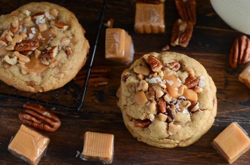 Salted caramel crunch cookies next to scattered caramels and toffee bits.