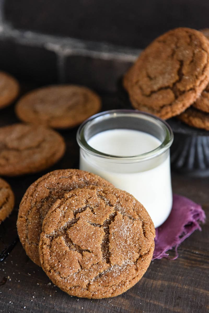 Gingerdoodle cookies stacked in front of a tumbler of milk with a napkin and more cookies int he background on a cooling rack.