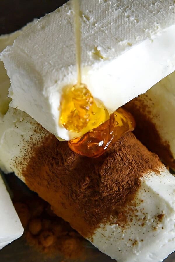 Honey is being drizzled into a bowl with goat cheese.