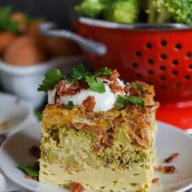 A slice of low carb breakfast casserole on a plate topped with sour cream and bacon bits.