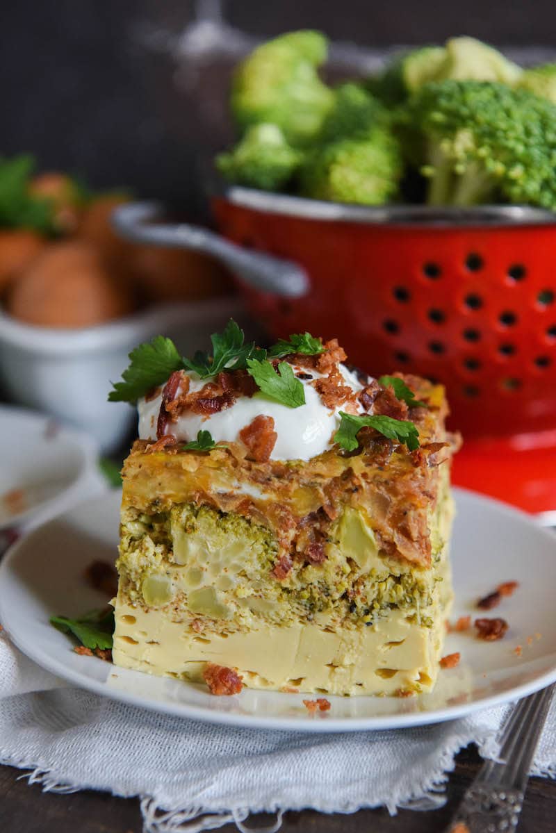 A slice of low carb breakfast casserole on a plate topped with sour cream and bacon bits.