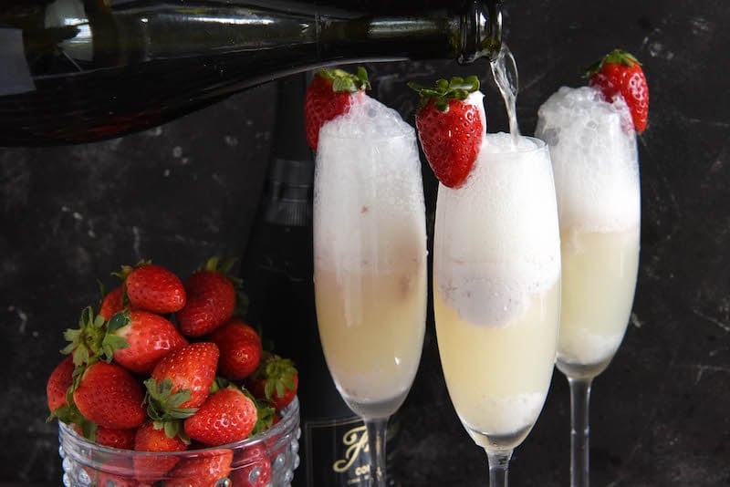 Three strawberry champagne floats in flute glasses garnished with fresh strawberries.