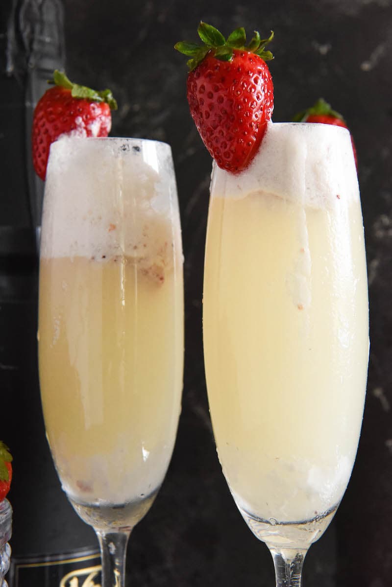 Two strawberry champagne floats in flute glasses garnished with fresh strawberries.