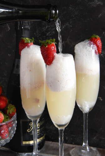 Three strawberry champagne floats in flute glasses garnished with fresh strawberries.