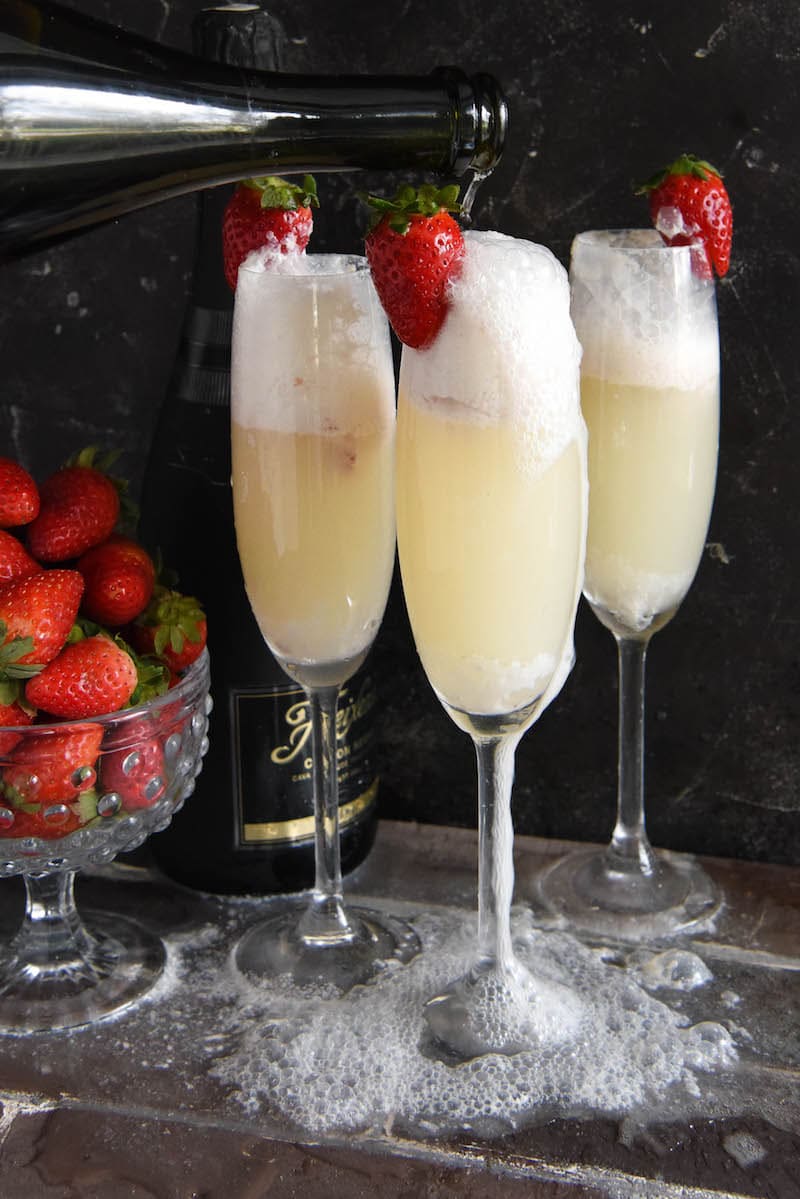 Three strawberry champagne floats in flute glasses garnished with fresh strawberries.