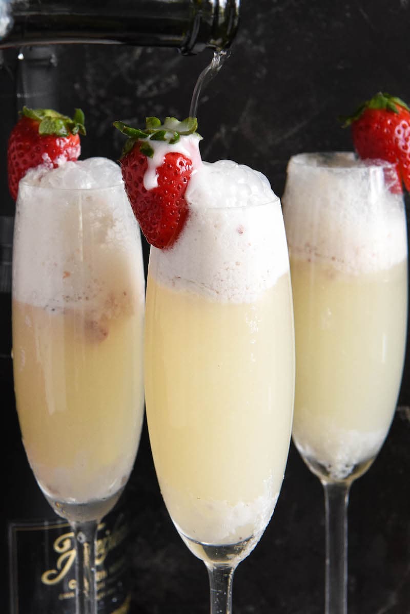 Three strawberry champagne floats in flute glasses garnished with fresh strawberries.