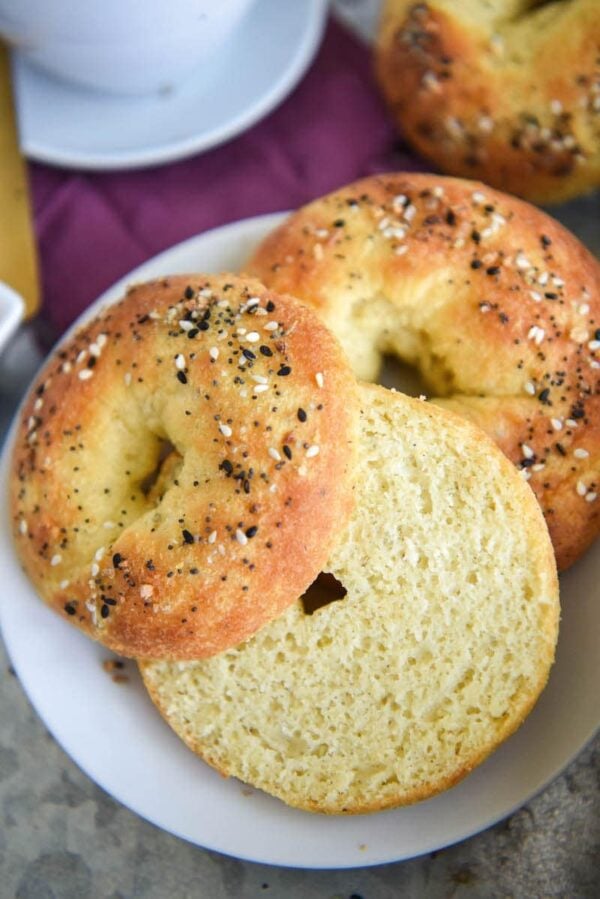 Keto Bagel sliced in half on top of another bagel with a white plate below.