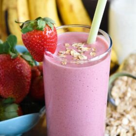 Banana Oatmeal Smoothie with a whole strawberry and a sprinkle of oats for garnish and fresh fruit in the background