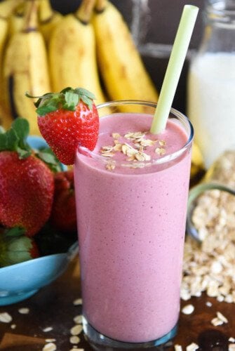 Banana Oatmeal Smoothie with a whole strawberry and a sprinkle of oats for garnish and fresh fruit in the background