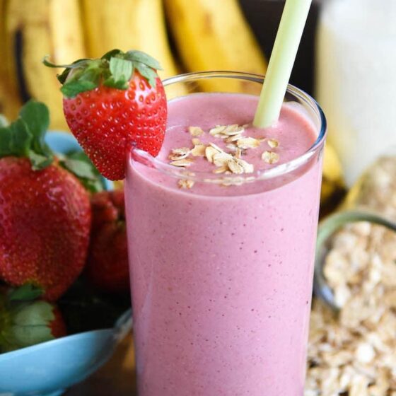 Banana Oatmeal Smoothie with a whole strawberry and a sprinkle of oats for garnish and fresh fruit in the background