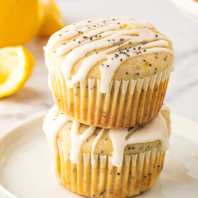 Two glazed lemon poppy seed muffins stacked on top of each other.