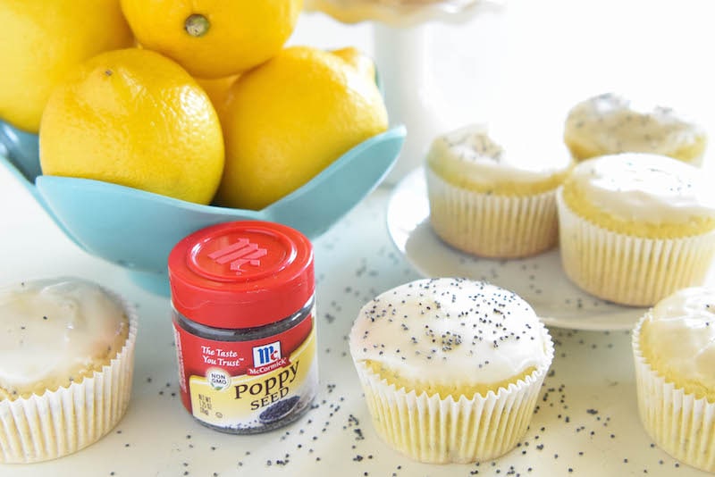 Lemon Poppyseed Muffins on a Counter with a Bowl of Fresh Lemons and a Jar of Poppy Seeds