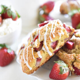 Strawberry shortcake scones on a white plate surrounded by fresh strawberries.