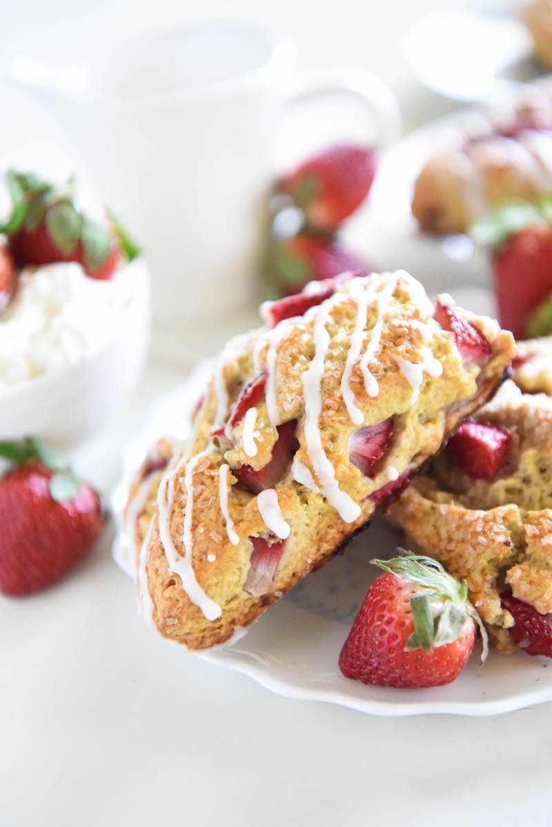 Strawberry shortcake scones on a white plate surrounded by fresh strawberries.