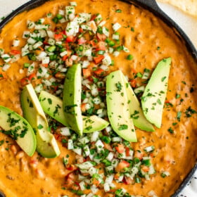 A skillet of taco beer cheese dip, garnished with avocado and other toppings.