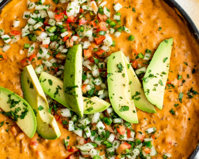 A skillet of taco beer cheese dip, garnished with avocado and other toppings.