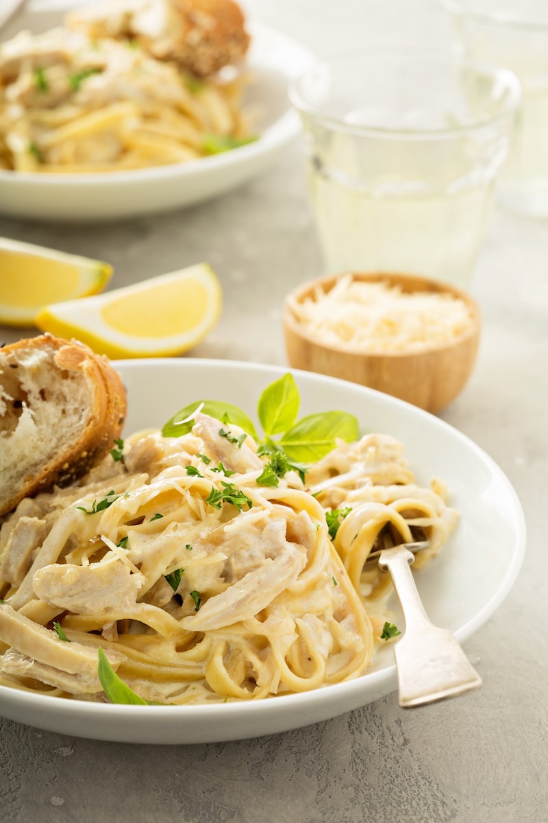 Instant pot chicken alfredo served into a large, shallow dish. Lemon wedges and parmesan are nearby on the table.