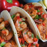 Three shrimp tacos on a platter with a bell pepper in back ground
