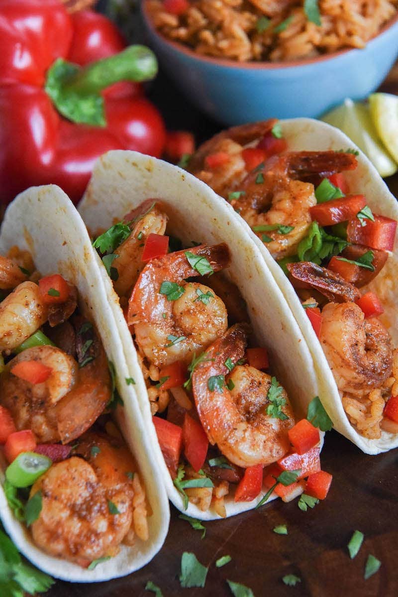 Three cajun shrimp tacos on flour tortillas with red bell pepper, cilantro, green onion, and tomatoes.