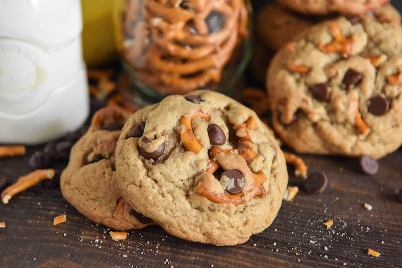 Three Chunky Monkey Cookies on a Table with a Jar of Pretzels