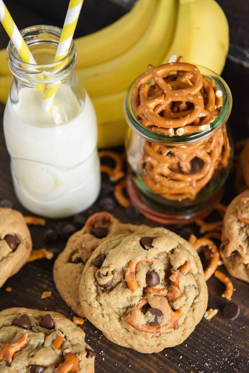 Five Chunky Monkey Cookies Beside a Glass of Milk, a Bunch of Bananas and a Jar of Pretzels