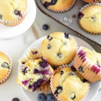 A Plate Full of Blueberry Muffins with More Muffins in a Pan Beside the Plate