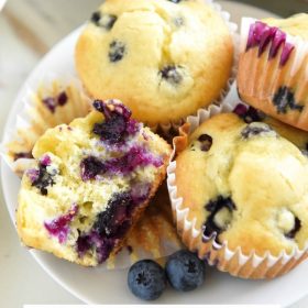 A Dessert Plate Holding Four Blueberry Muffins with One Split in Half to Show the Fluffy Interior