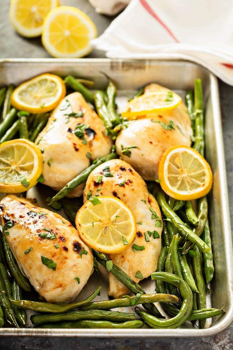 Chicken breasts, green beans and lemons on a metal sheet pan with a tea towel. 