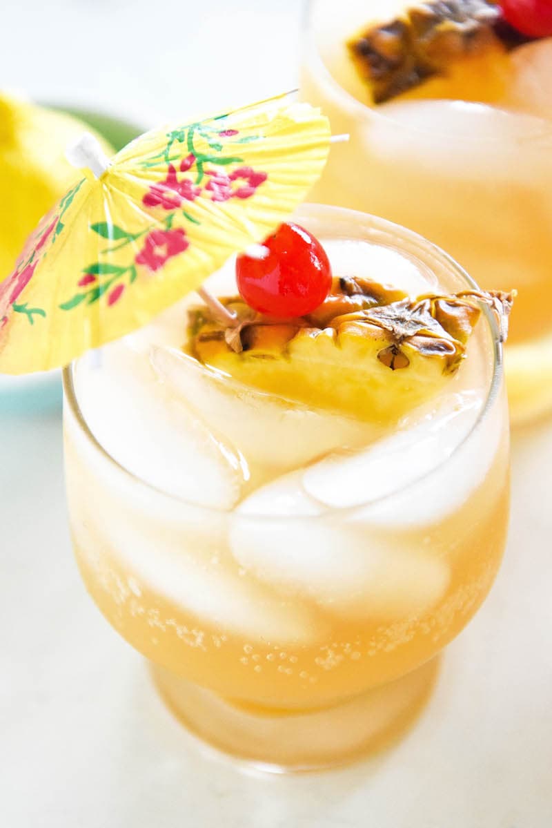 Glasses of sparkling pineapple punch garnished with cherries, pineapple slices, and a cocktail umbrella.